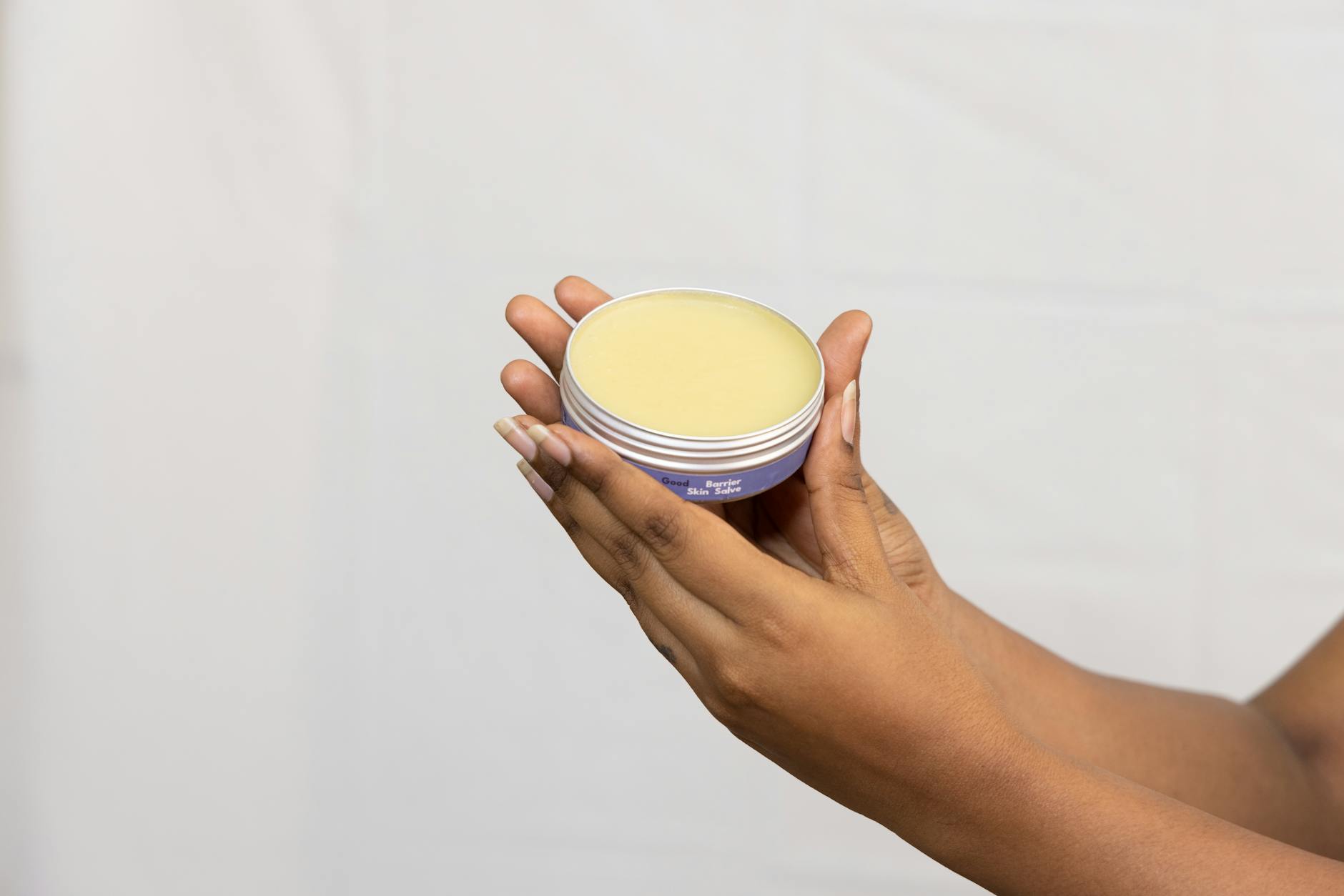 A close-up of hands holding a jar of moisturising cream against a neutral backdrop