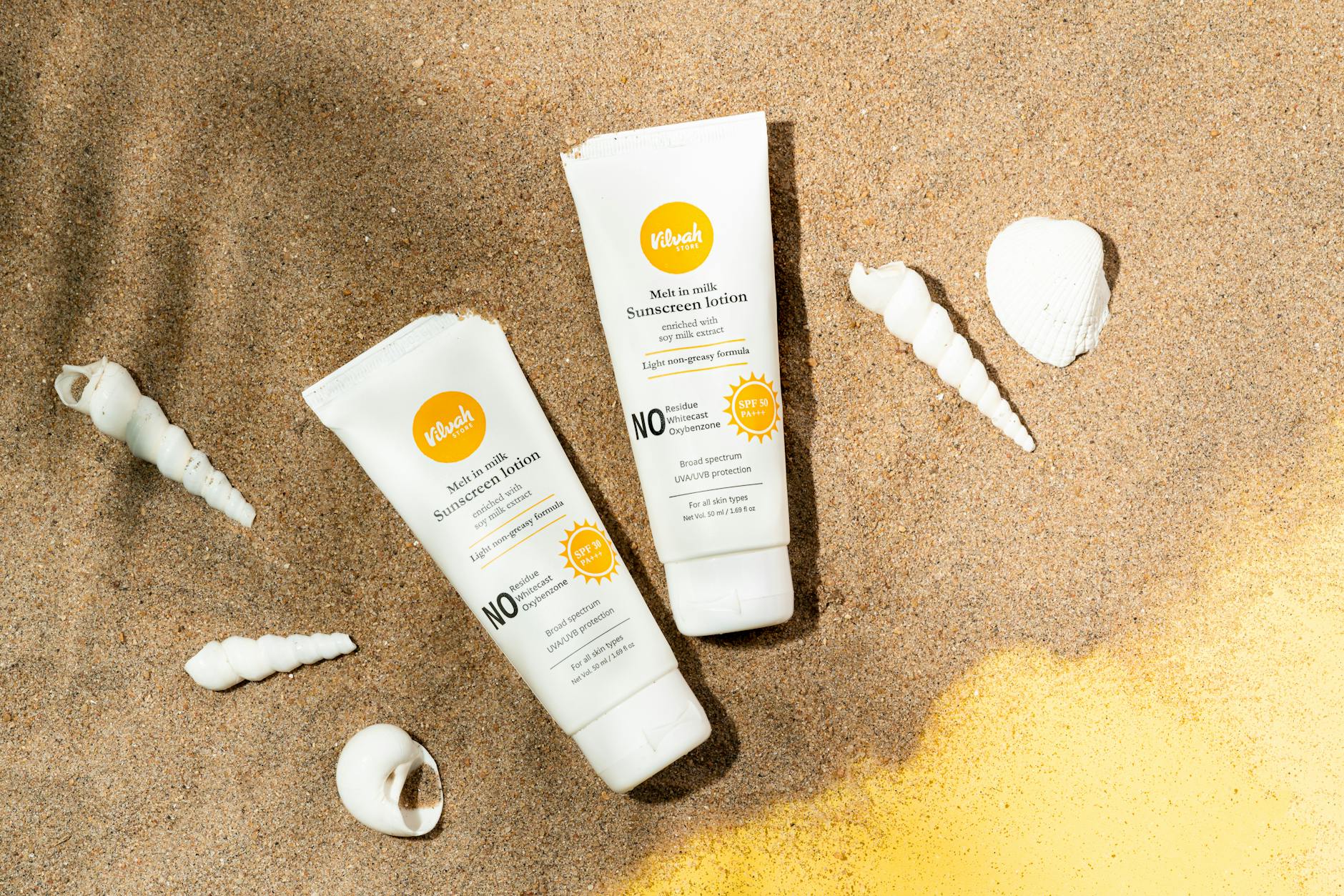 Two sunscreen lotion tubes on sandy beach alongside seashells