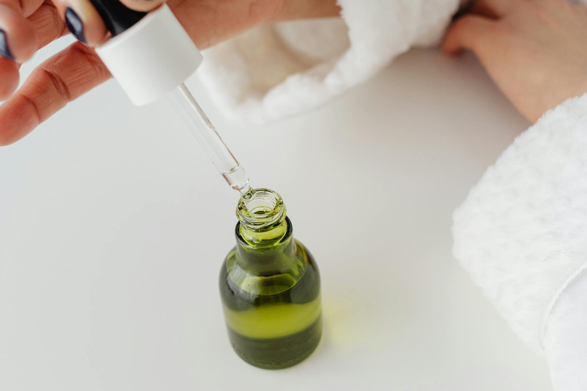 Close-up of hands holding a dropper over a serum bottle