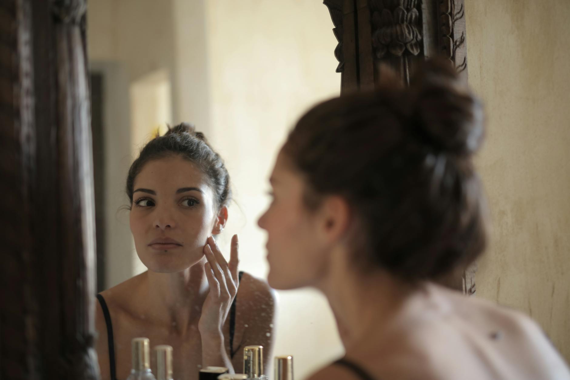 A woman examining her facial skin in a mirror as part of her skincare assessment
