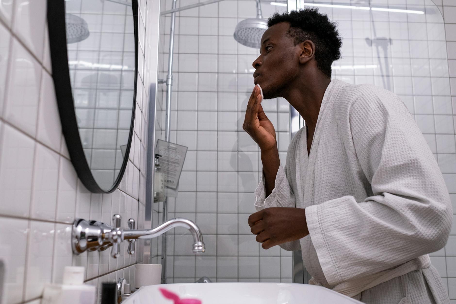 Man applying skincare products as part of a daily morning routine in front of a bathroom mirror