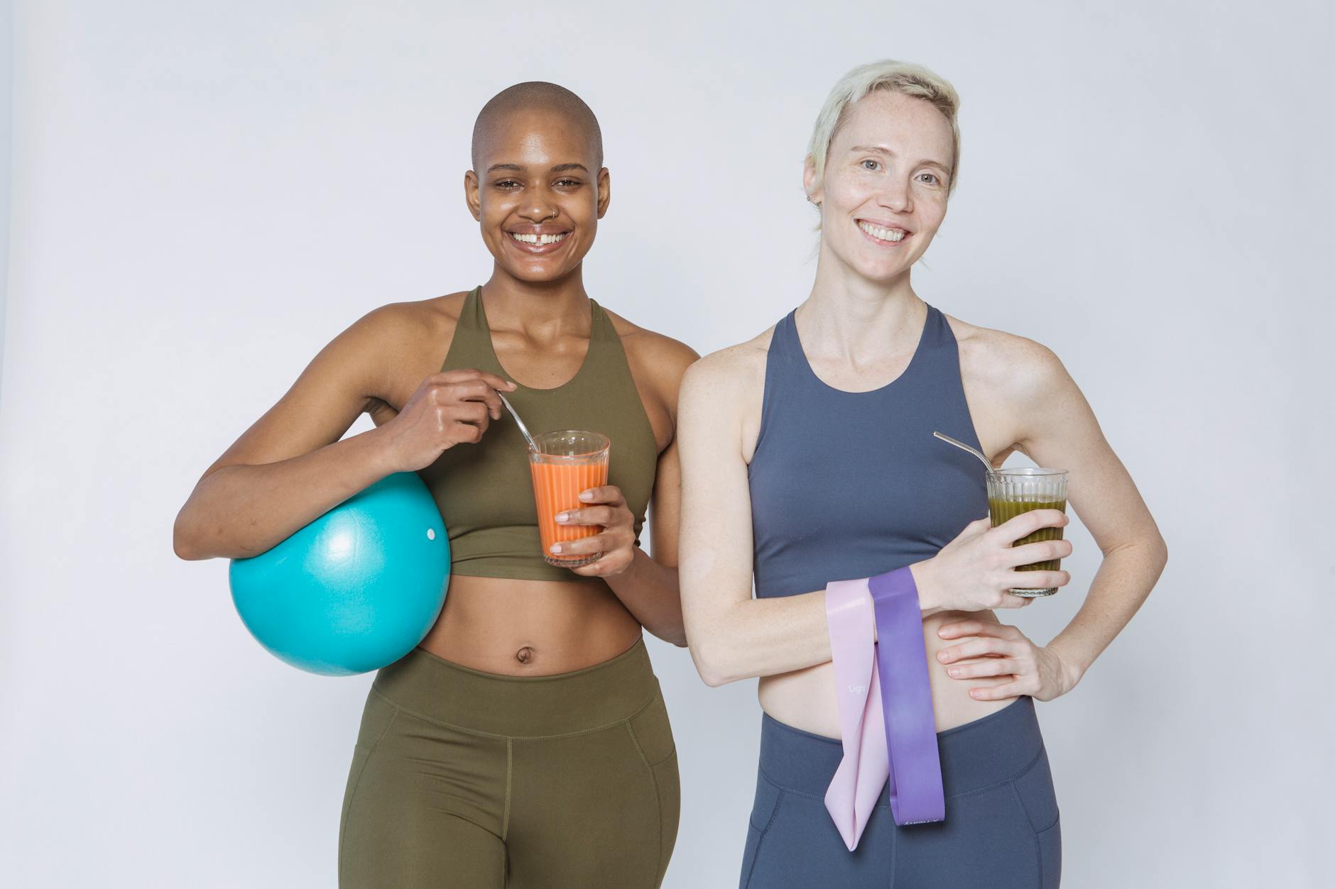 Two women smiling with smoothies and fitness gear, representing healthy lifestyle habits that support skin quality