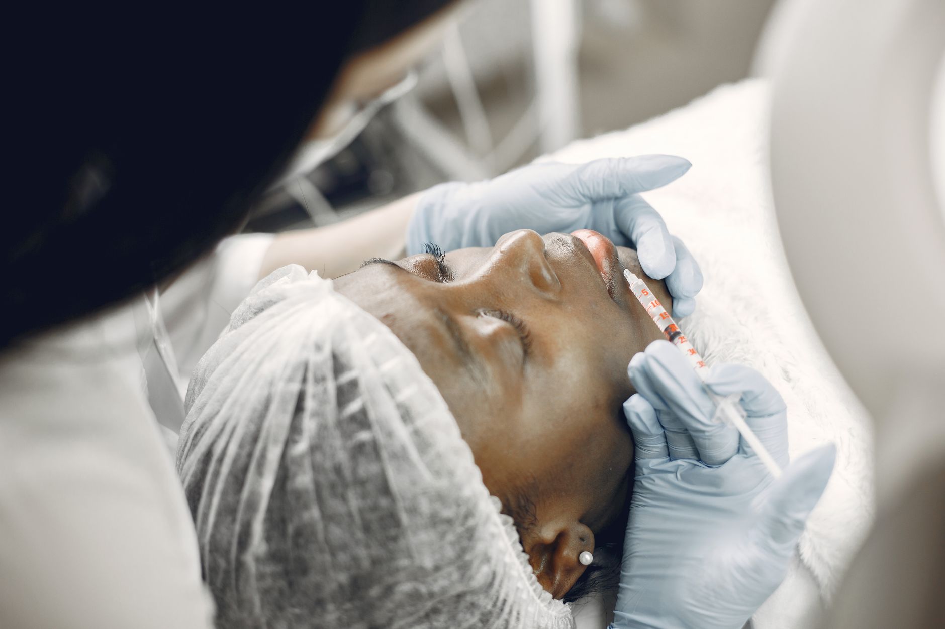 A practitioner administering a dermal filler injection to a patient's lips in a clinic