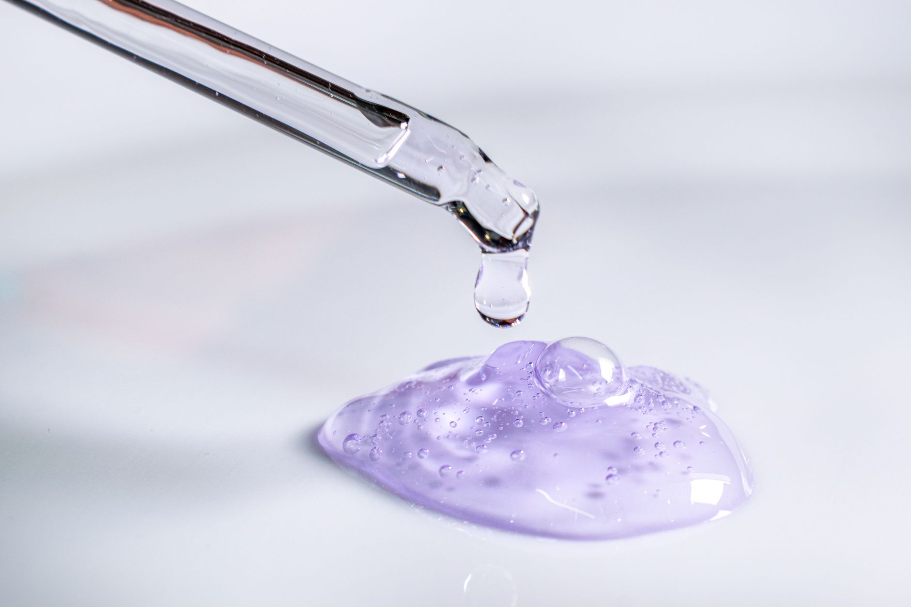 A pipette releasing a drop of serum, evoking laboratory skincare science